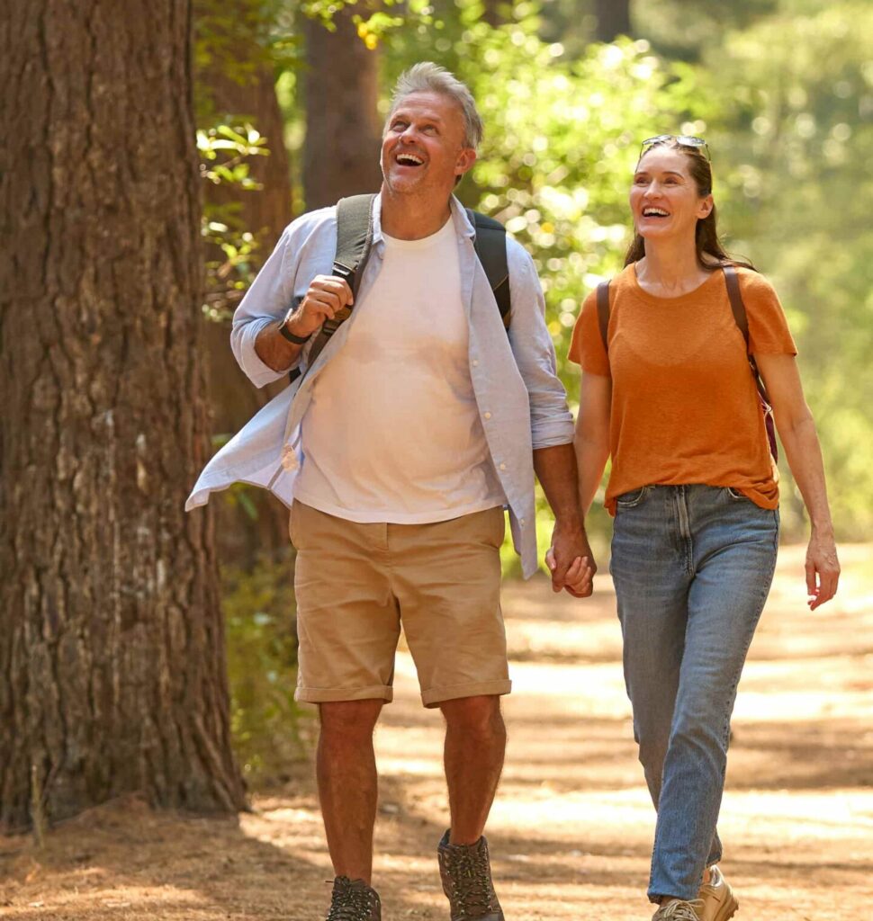 Senior Retired Couple Holding Hands Hiking Along Trail In Countryside