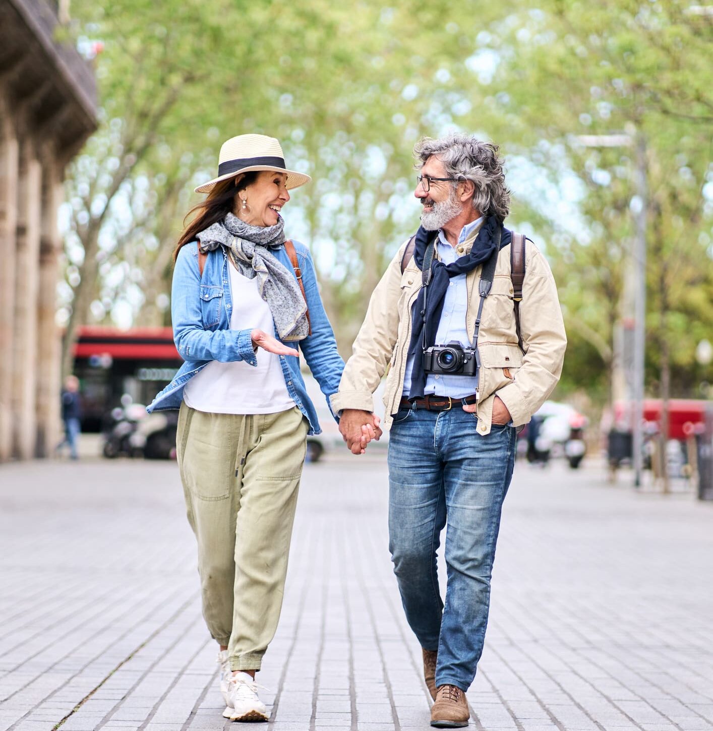 Happy adult Caucasian tourist couple looking at each other walking holding hand for street in city