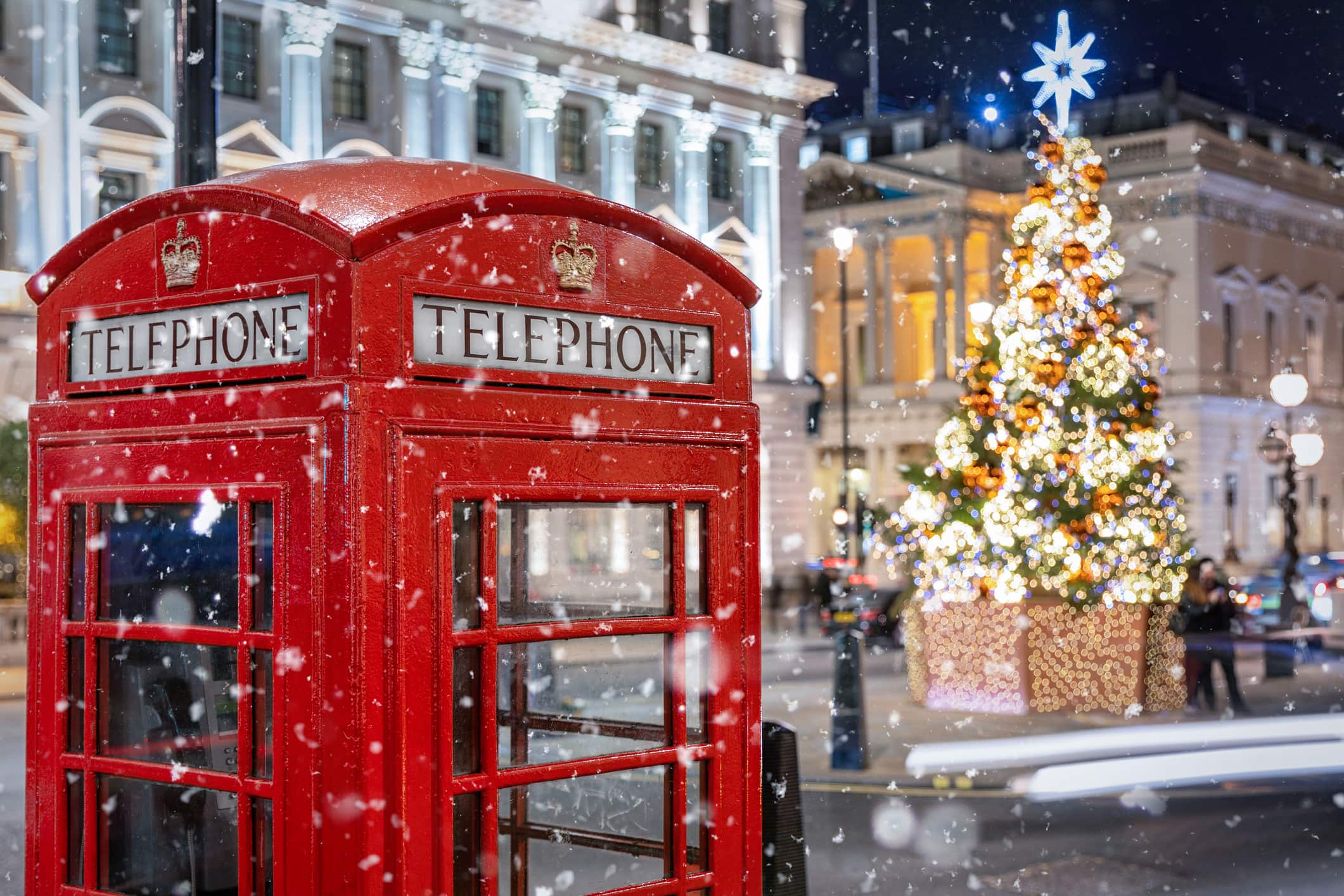 Red Telephone Booth Against Christmas Tree In Illuminated City During Snowfall